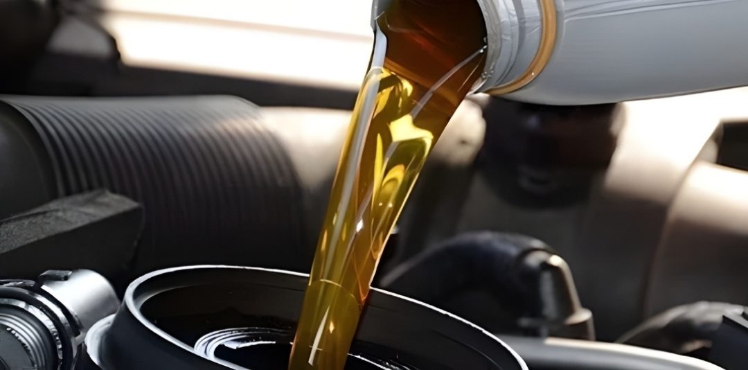 Close-up of amber engine oil being poured from a bottle into a car's oil fill opening.